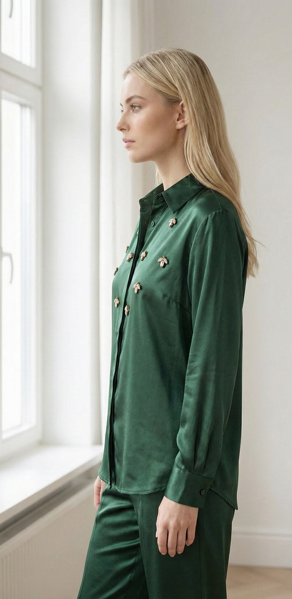 Blonde woman in green satin blouse and pants with bee embellishments standing by bright window