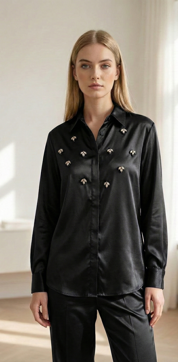 Woman wearing a black satin shirt with decorative bee embellishments and matching black pants in bright room