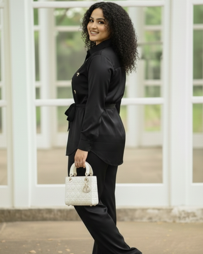 Woman in a black outfit holding a white handbag in front of a large window.